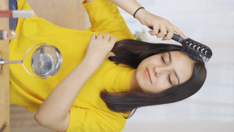 Vertical-video-of-Young-woman-combing-her-hair.-Hair-care.